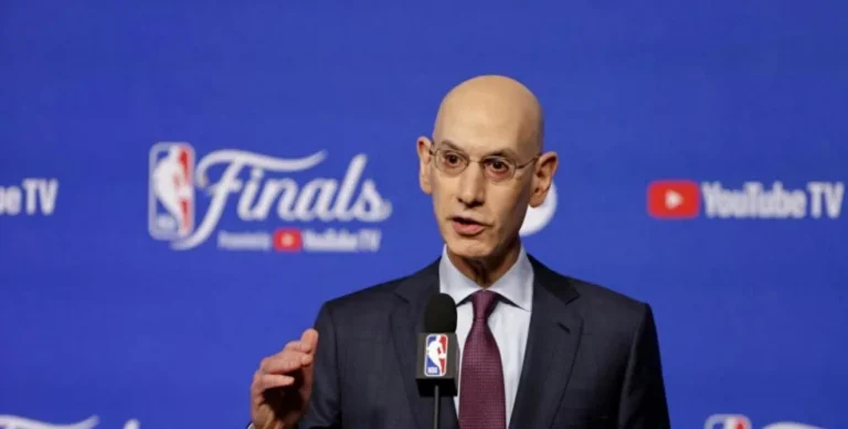 NBA commissioner Adam Silver speaking at a microphone in front of an NBA Finals backdrop.