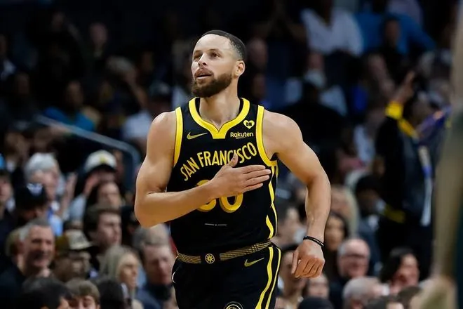 Stephen Curry jogging back up court in the Golden State Warriors black and gold San Francisco jersey, hand on his chest, with a full crowd behind him.