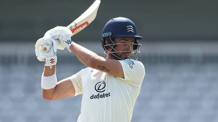 Middlesex opener Max Holden driving the ball square on the off side in white kit and a navy helmet